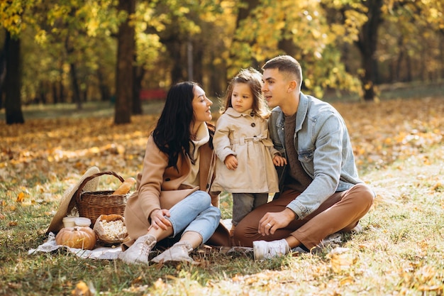 Portret van een gelukkig jong gezin dat samen op een plaid zit in het herfstpark