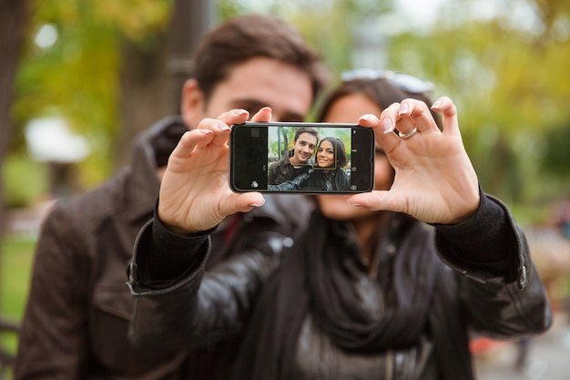 Portret van een gelukkig jong koppel selfie foto maken op smartphone buitenshuis. focus op het smartphonescherm