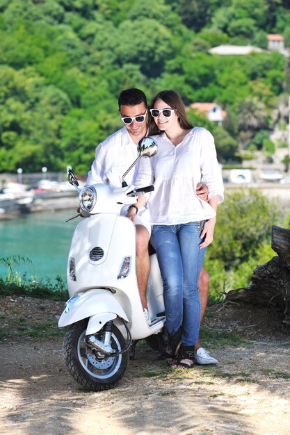 Portret van een gelukkig jong liefdespaar op een scooter die zich in de zomer in een park vermaakt