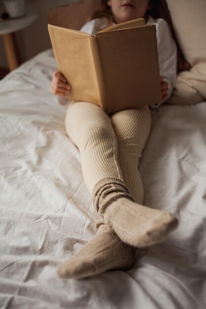 Foto portret van een gelukkig kind een mooi krullend meisje leest een boek in haar bed een gezellig huis