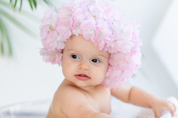 Portret van een gelukkig klein kind meisje in een lichte kamer thuis in een mooie hoed gemaakt van bloemen