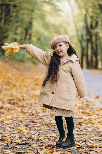 Portret van een gelukkig klein meisje in een beige jas en baret die gele esdoornbladeren vasthoudt en tijd doorbrengt in het herfstpark