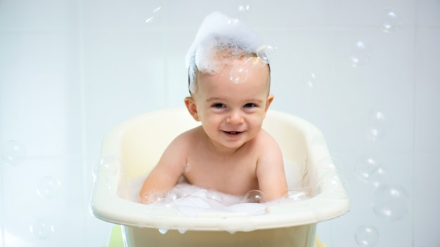 Portret van een gelukkig lachend jongetje met zeepschuim en shampoo op het hoofd in bad.