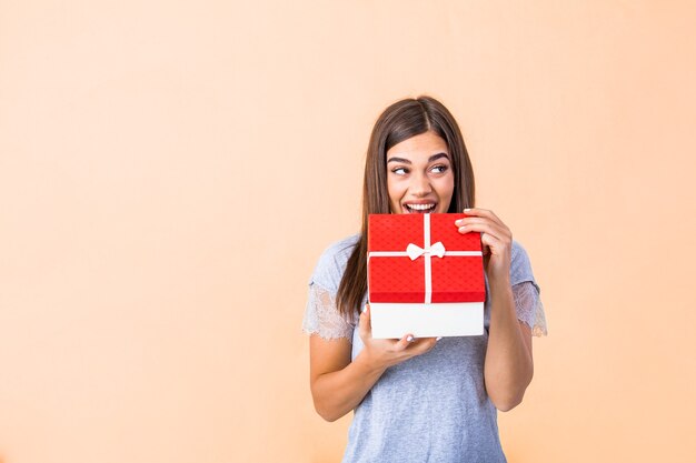 Portret van een gelukkig lachend meisje dat een doos van de kerstmisgift opent die over geel wordt geïsoleerd