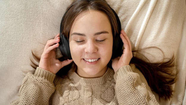 Foto portret van een gelukkig lachend tienermeisje dat muziek luistert en ontspant in bed