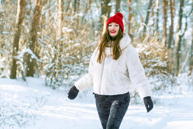 Portret van een gelukkig lachende jonge blanke vrouw met een rode hoed in het besneeuwde bos Zonnige dag in het winterpark