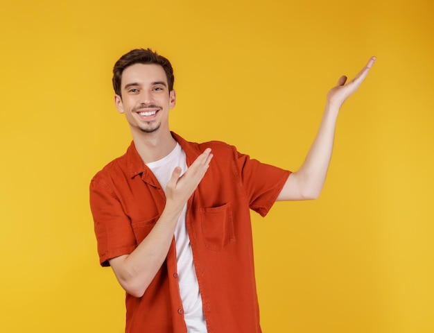 Portret van een gelukkig lachende jonge man die uw tekst of product presenteert en toont geïsoleerd op gele achtergrond
