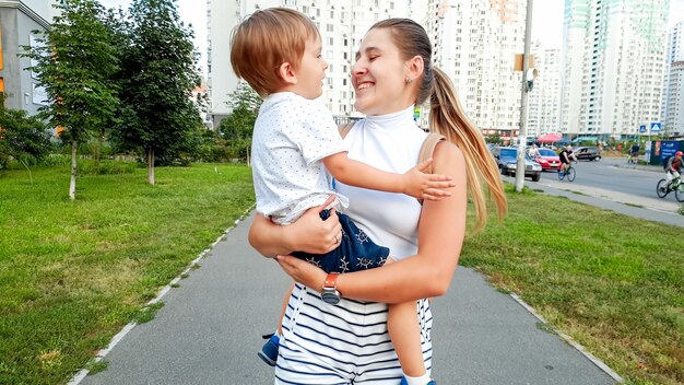 Portret van een gelukkig lachende jonge vrouw die haar peuterzoon knuffelt en op straat in de stad loopt