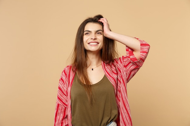 Portret van een gelukkig lachende jonge vrouw in casual kleding die opzij kijkt, hand op het hoofd zet geïsoleerd op pastel beige muur achtergrond. Mensen oprechte emoties, lifestyle concept. Bespotten kopie ruimte.