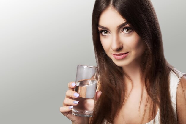 Portret van een gelukkig lachende jonge vrouw met een glas vers water