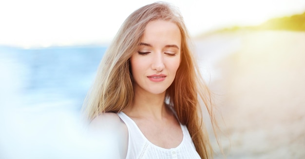 Portret van een gelukkig lachende vrouw in gelukzaligheid op oceaanstrand genietend van de natuur tijdens reisvakanties buitenshuis. Kijk door witte vage bloemen.