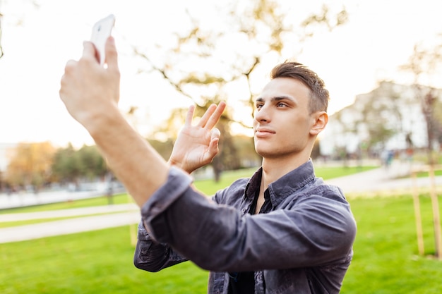 Portret van een gelukkig man, in zonnebril, permanent in het park met een smartphone.