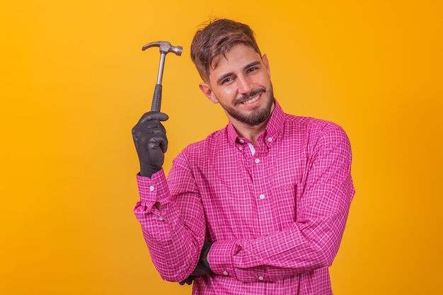 Portret van een gelukkig manusje van alles die hamer over gele achtergrond houdt.