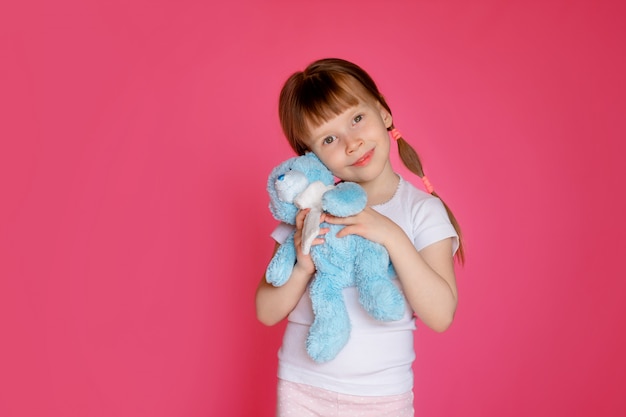 portret van een gelukkig meisje 5-6 jaar oud op een roze muur met een teddybeer in haar handen, het kind bereidt zich voor op bed