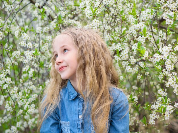 Portret van een gelukkig meisje in een denim shirt in de buurt van een kersenboom.