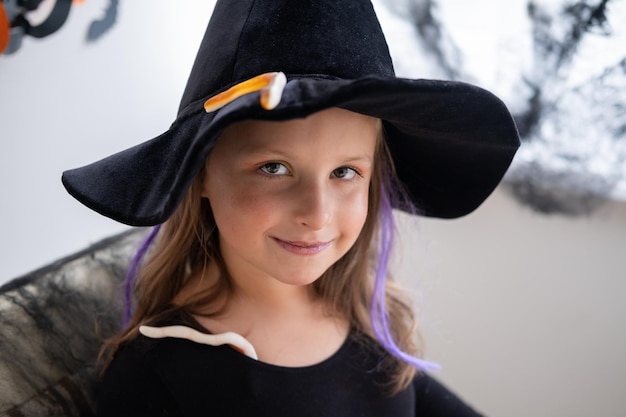 Foto portret van een gelukkig meisje met een zwarte heksenhoed die thuis halloween viert?