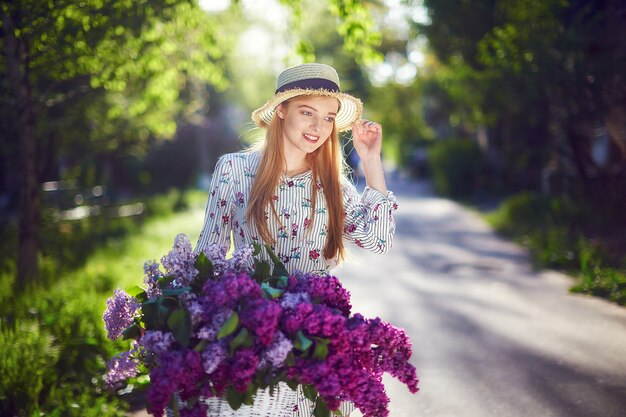 Portret van een gelukkig mooi jong meisje met vintage fiets en bloemen op de achtergrond van de stad in het zonlicht buiten. Fiets met mand vol bloemen. Actief vrijetijdsconcept.