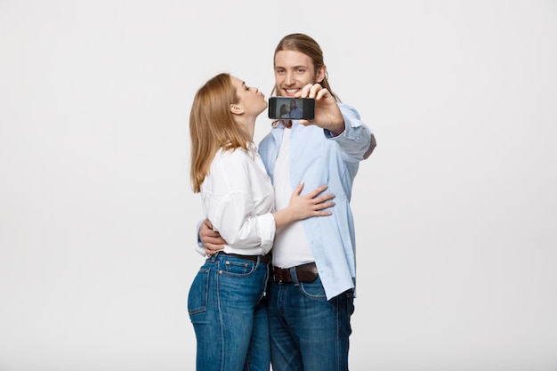 Portret van een gelukkig paar dat selfie-foto maakt met smartphone over geïsoleerde witte studioachtergrond