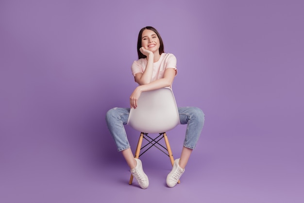 Portret van een gelukkig positief meisje zit stoel geniet van vrije tijd op paarse muur
