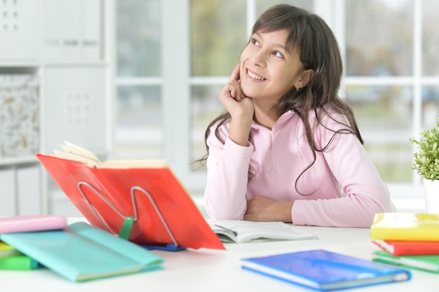 Portret van een gelukkig schoolmeisje dat aan het bureau zit en studeert