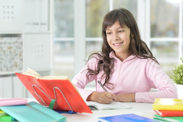 Portret van een gelukkig schoolmeisje dat aan het bureau zit en studeert