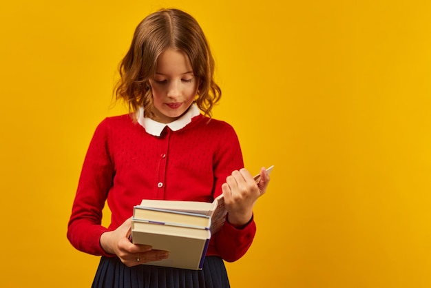 Portret van een gelukkig schoolmeisje dat een boek over gele studio leest