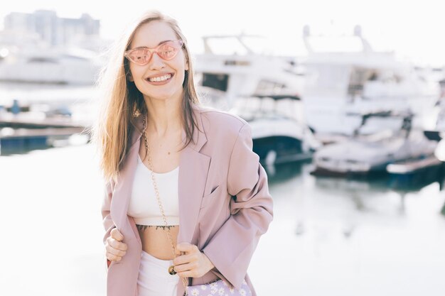 Foto portret van een gelukkig vrolijk emotioneel reizend meisje in modieuze kleren bij jachten en water