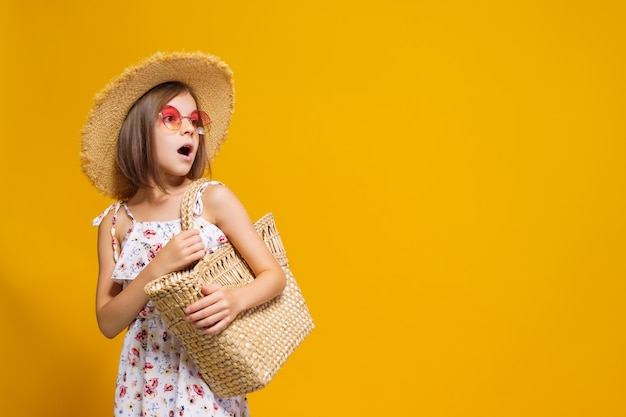 Portret van een gelukkig vrolijk meisje in de strozak van de de zomerhoedzonnebril over gele achtergrond