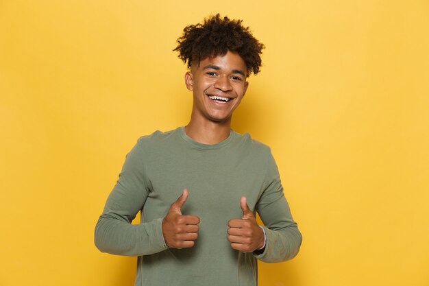 Portret van een gelukkige Afrikaanse man met een stijlvol afro-kapsel met duimen omhoog, geïsoleerd op gele achtergrond