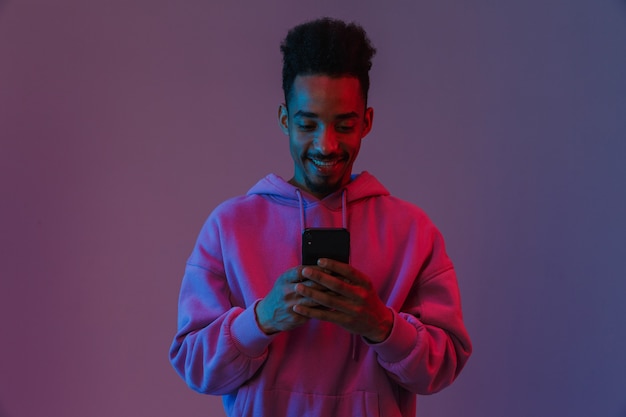 Portret van een gelukkige Afro-Amerikaanse man in een kleurrijke hoodie die een videogesprek voert op een mobiele telefoon die over een violette muur wordt geïsoleerd