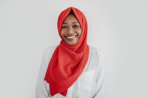 Portret van een gelukkige Afro-Amerikaanse moslimvrouw in hijab die kijkt en glimlacht naar de achtergrond van de lichte studio van de camera