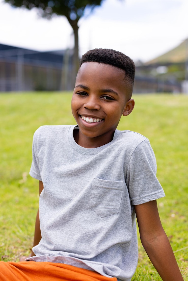 Foto portret van een gelukkige afro-amerikaanse schooljongen die op het gras zit op school