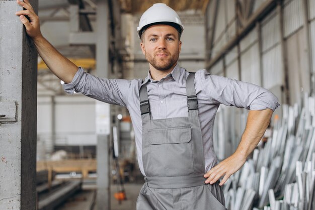 Foto portret van een gelukkige arbeider in een grijs uniform en een witte helm die zich voordeed op de achtergrond van de fabrieksproductie