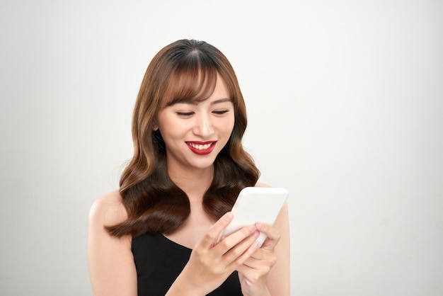 Portret van een gelukkige Aziatische onderneemster die mobiele telefoon met behulp van die over witte achtergrond wordt geïsoleerd