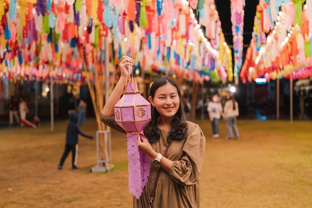 Foto portret van een gelukkige aziatische vrouw met een handgemaakte papieren lantaarn voor het inleveren van de jaarlijkse traditie van het hangen van lantaarns in noord-thailand 's nachts bij de phra that hariphunchai-tempel, lamphun