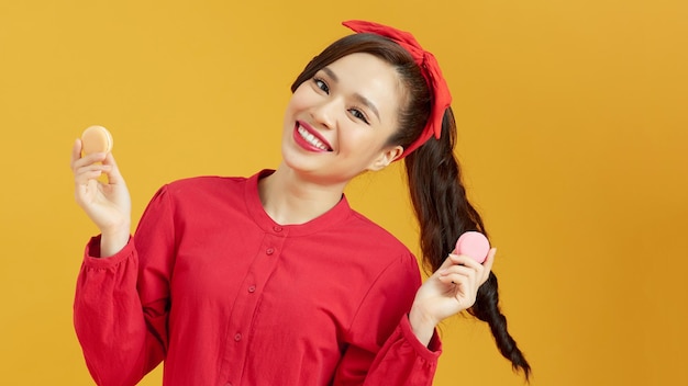 Portret van een gelukkige Aziatische vrouw met macaron die naar de camera kijkt