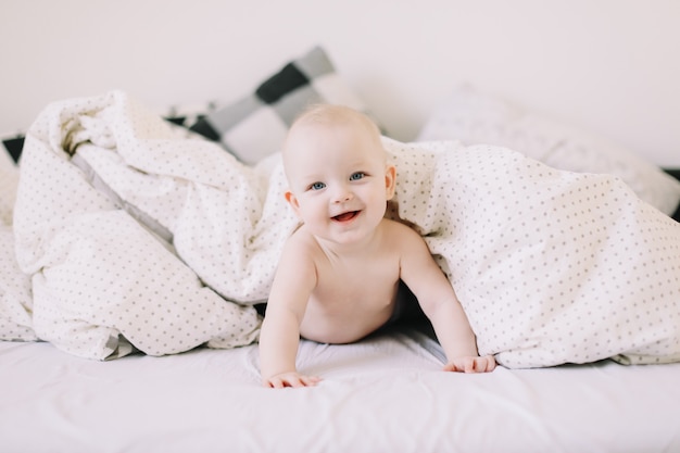 Portret van een gelukkige baby die zich onder de witte deken verstopt.