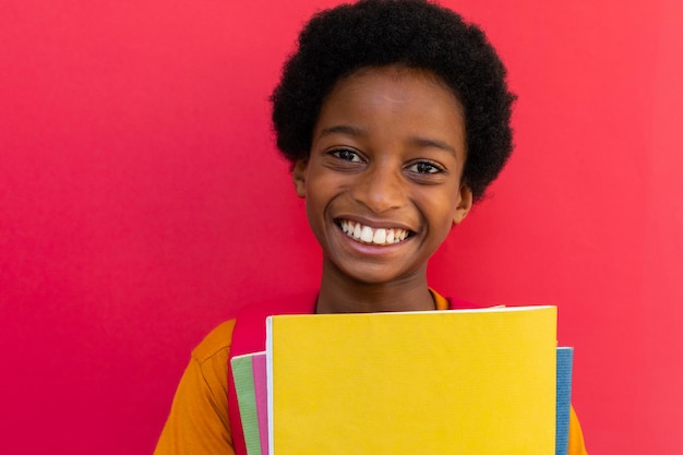 Portret van een gelukkige biraciale schooljongen met boeken in een geel t-shirt op een roze achtergrond