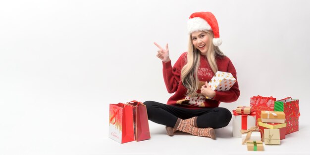 Portret van een gelukkige blanke jonge vrouw in een kerstmuts met geschenkdoos en winkelen