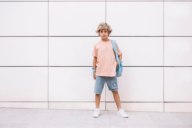 Portret van een gelukkige blanke jongen met een schooltas, wachtend op zijn klasgenoten om naar school te gaan. eerste lesdag.