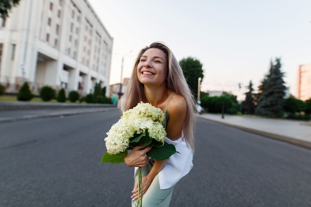 Portret van een gelukkige emotionele vrouw met bloemen in straatstijl blonde vrouw met boeket hortensia