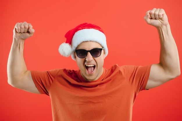 Portret van een gelukkige en opgewonden man in een kerstmuts, die zich verheugt en iets wint, nieuwjaar viert, staande over rode achtergrond