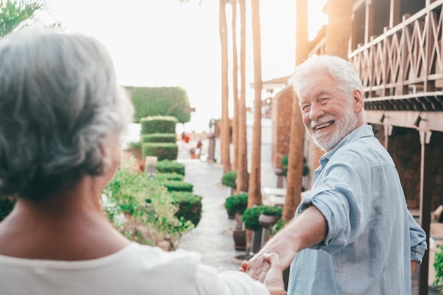 Portret van een gelukkige en schattige senior die de hand vasthoudt van een oude gepensioneerde vrouw die wandelt en nieuwe plaatsen bezoekt samen met de zonsondergang op de achtergrond Paar dat plezier heeft in het park