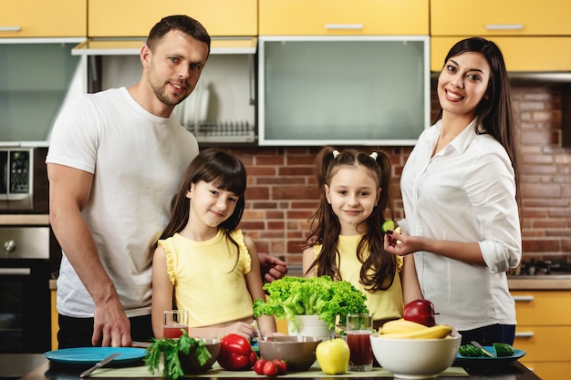 Portret van een gelukkige familie, moeder vader en twee dochters, koken salades in keuken thuis. Gezond eten concept