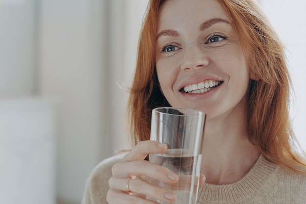 Portret van een gelukkige, gezonde gembervrouw met transparant glas puur mineraalwater