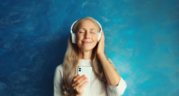 Portret van een gelukkige glimlachende vrouw van middelbare leeftijd die naar muziek luistert in koptelefoon met smartphone