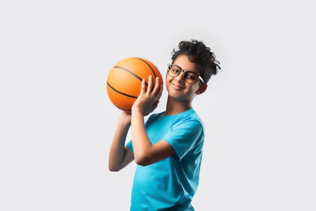 Portret van een gelukkige indiase aziatische jongen die basketbal speelt of vasthoudt tegen een witte muur