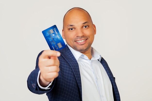 Portret van een gelukkige jonge Afro-Amerikaanse zakenman man met een creditcard met een blij gezicht, staat en glimlacht met een zelfverzekerde glimlach met tanden.