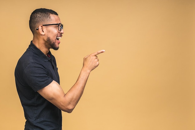 Portret van een gelukkige jonge afro-amerikaanse zwarte man met een casual glimlach die opzij wijst met een vinger geïsoleerd over een beige achtergrond