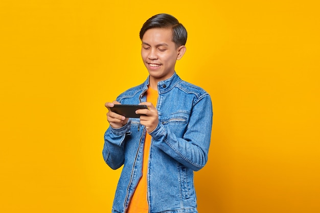 Portret van een gelukkige jonge Aziatische man die een videogame speelt op een mobiele telefoon